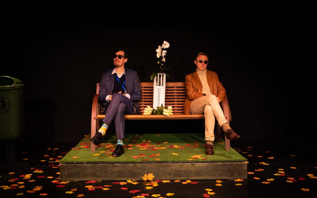Jörn Kolpe und Martin Müller sitzen auf einer Bank, am Kunstrasen liegen herbstliche Blätter.