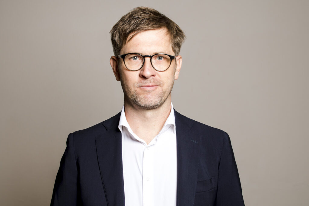 Joachim Brandl mit Brille, kurzen braunen Haaren, weißem Hemd und offenem schwarzem Sakko 