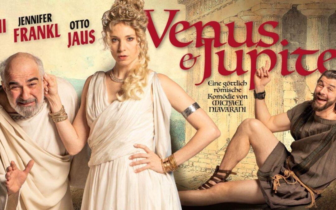 Venus (Jenny Frankl) hält Jupiter (Michael Niavarani) am Ohr. Otto Jaus zeigt als in einen Sklaven verwandelten Gott Apoll lachend auf den Titel des Stücks: "Venus & Jupiter"