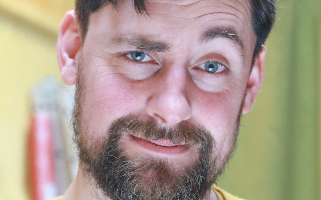 headshot of Feargus Woods Dunlop, wearing a yellow shirt and looking quizzically