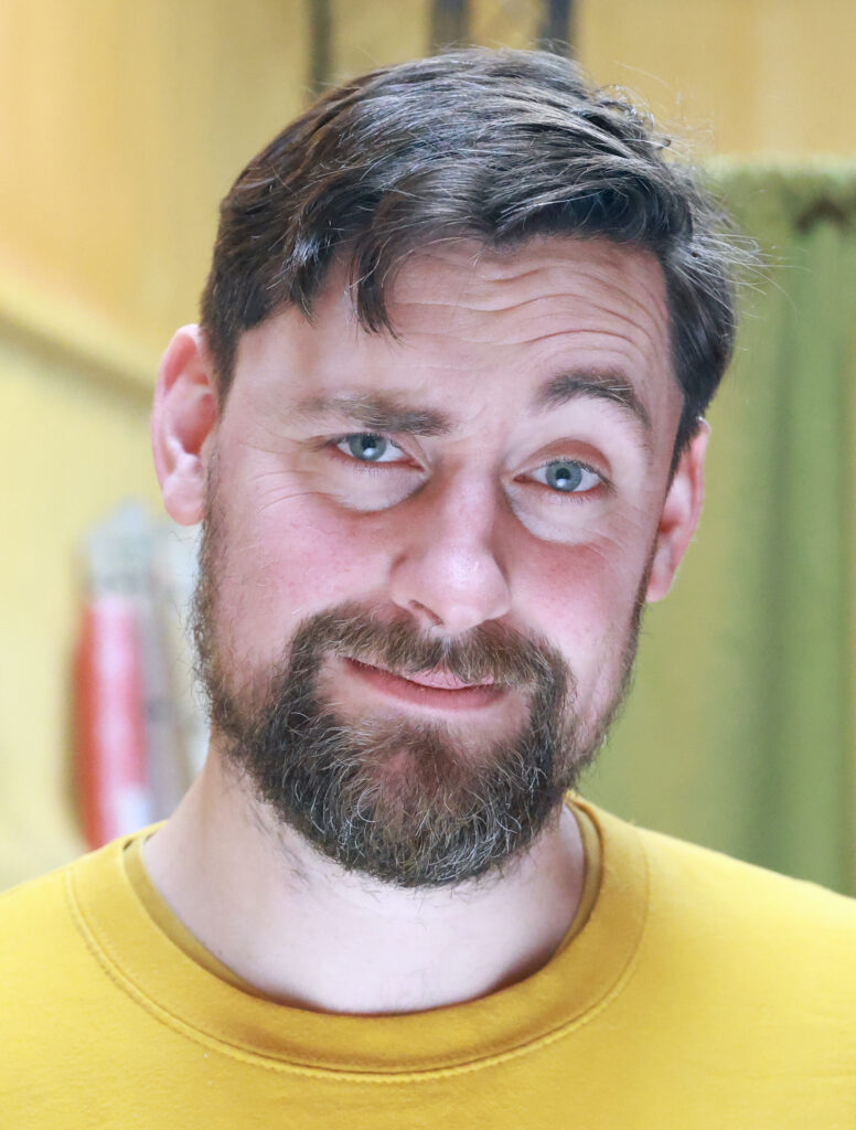 headshot of Feargus Woods Dunlop, wearing a yellow shirt and looking quizzically 