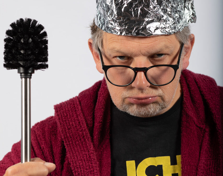 Mit trotzigem Blick sieht Severin Groebner in die Kamera. Er ist ein älterer, weißer Mann mit hellem, kurzem Bart und grauen Haaren. Auf seinem Kopf trägt er eine Krone aus Alufolie, seine dunkle Brille ist ihm die Nase hinabgerutscht. Seine rechte Faust ist erhoben und hält eine Klobürste wie ein Zepter. Unter einem roten Frotteebademantel lugt ein schwarzes T-Shirt mit der gelben Aufschrift "Ich Wars" hervor.